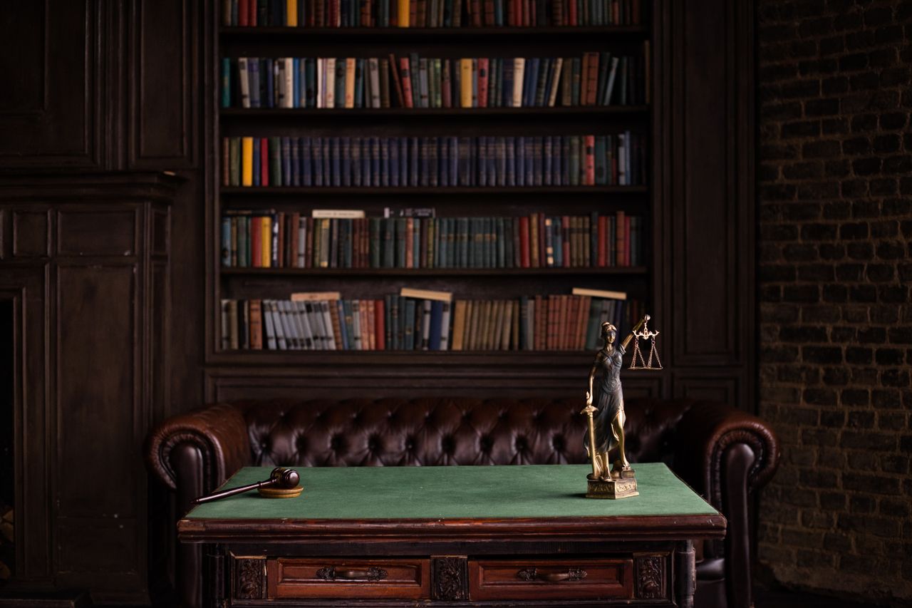 services-03 A classic study room with shelves of books, a gavel, and Lady Justice figurine on a green table.
